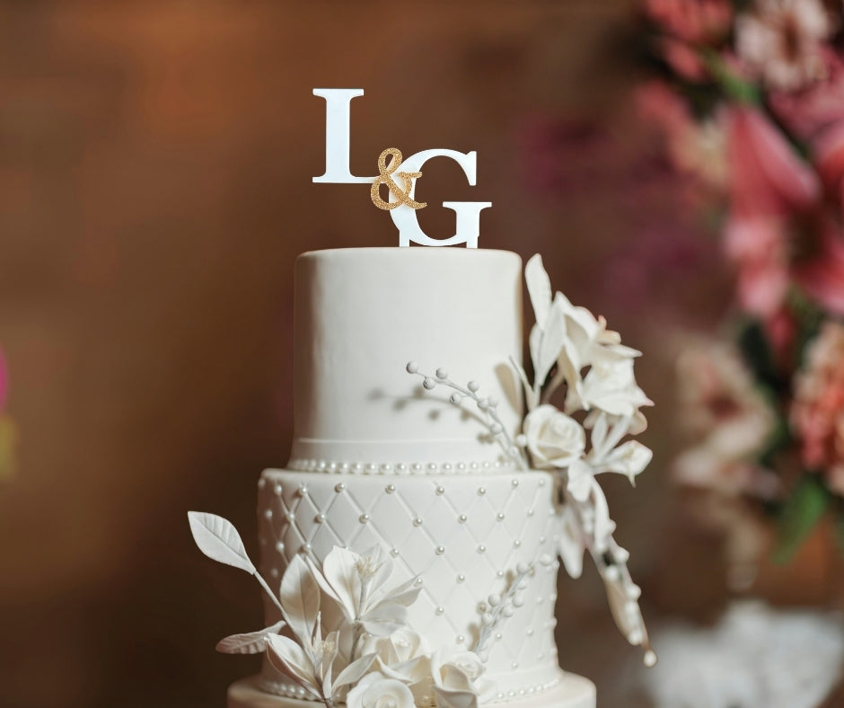 White wedding cake with floral decorations topped with personalized initials cake topper L & G in white and gold.
