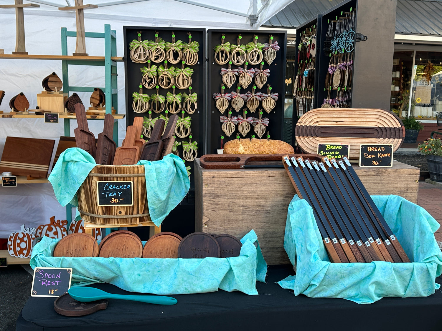 Variety of Zig's Woodshed products set up at a fall festival.  Products include spoon rest, bread bow knife, bread board, cracker tray, laser cut ornaments, cutting boards, and salt cellars.