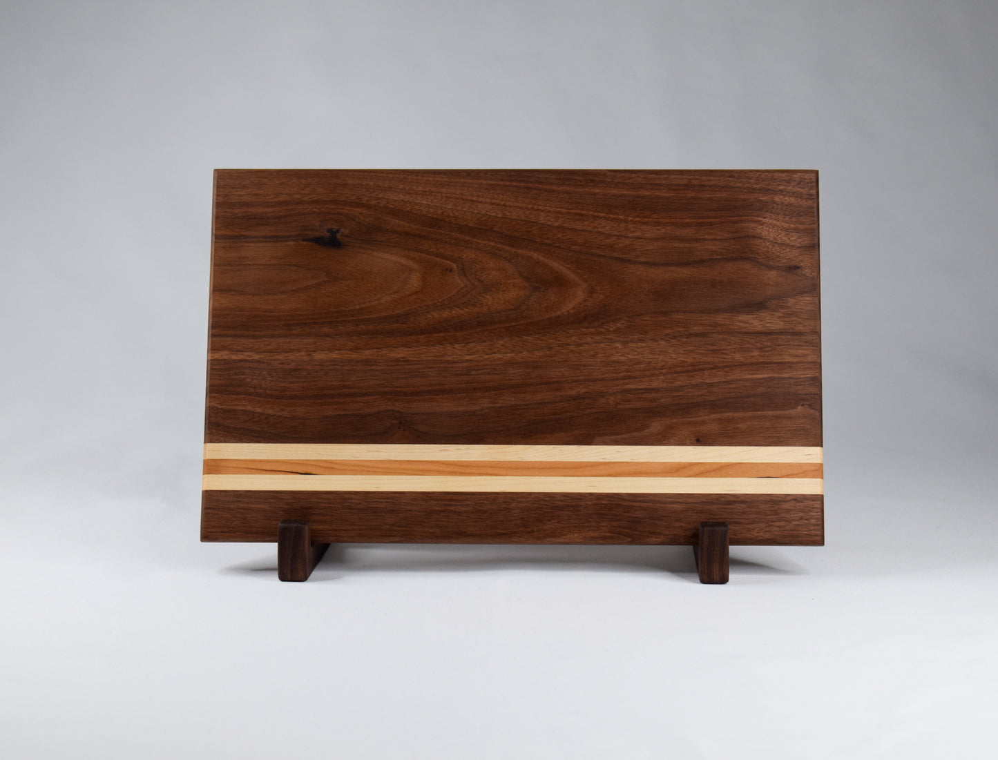 This striped cutting board is the perfect addition to any kitchen with its simple alternating stripes of maple and cherry hardwoods against a walnut backdrop. Complete with non-skid rubber feet for a sturdy cutting surface, this cutting board will not only provide functionality for the chef in your home, but will also serve as a statement piece in the kitchen.