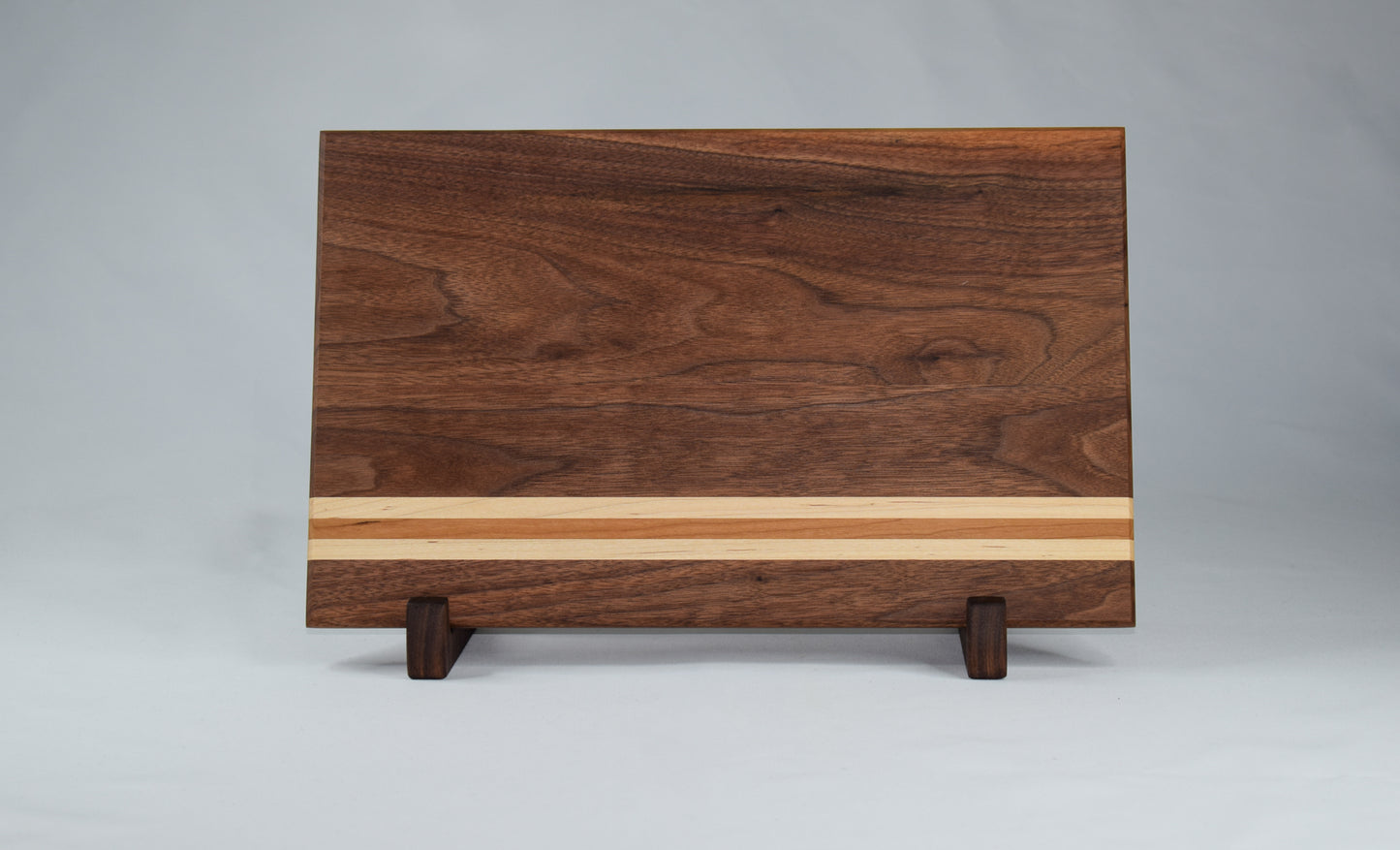 This striped cutting board is the perfect addition to any kitchen with its simple alternating stripes of maple and cherry hardwoods against a walnut backdrop. Complete with non-skid rubber feet for a sturdy cutting surface, this cutting board will not only provide functionality for the chef in your home, but will also serve as a statement piece in the kitchen.