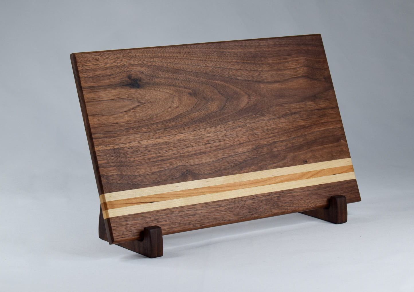 This striped cutting board is the perfect addition to any kitchen with its simple alternating stripes of maple and cherry hardwoods against a walnut backdrop. Complete with non-skid rubber feet for a sturdy cutting surface, this cutting board will not only provide functionality for the chef in your home, but will also serve as a statement piece in the kitchen.