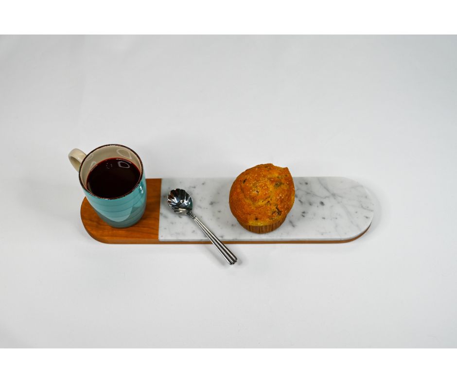A marble and wood serving board in an oval shape - locally made in Georgia. The serving board is being displayed with coffee and a muffin.