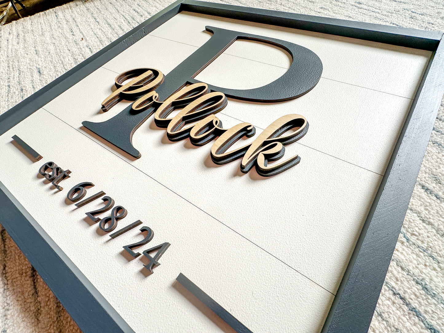 Up close shot of custom wedding sign. Sign features a faux shiplap background with a last name over a monogram and a wedding date.