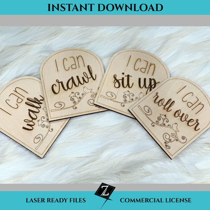 Laser-engraved wooden milestone signs reading “I can walk,” “I can crawl,” “I can sit up,” and “I can roll over,” each with floral and bird designs on arched wood pieces, displayed on soft faux fur.