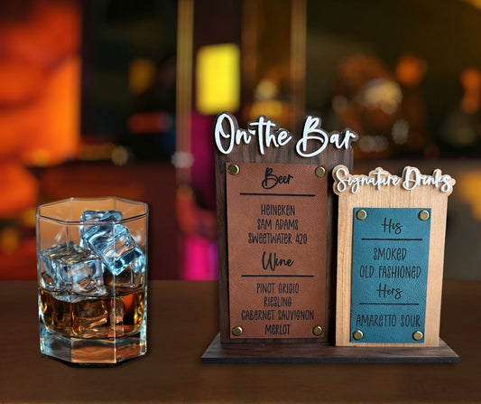 Wedding bar menu sign with layered wooden panels reading On the Bar and Signature Drinks, listing beer, wine, and cocktail options, displayed next to a glass of whiskey with ice.
