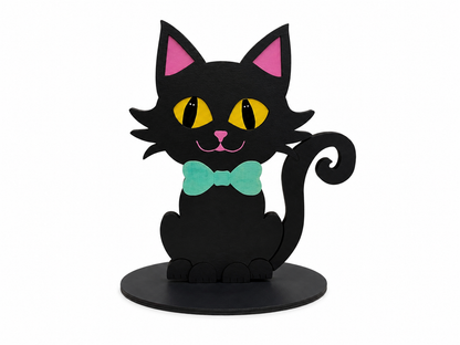 A stylized black cat figurine or sign with pink inner ears, yellow eyes, a mint green bow tie, and a black circular base, shown on a plain white background.