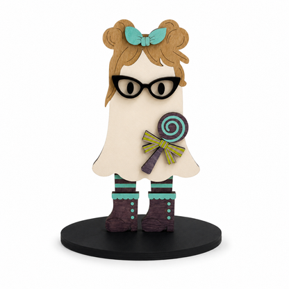 A stylized wooden ghost figurine with brown hair in a teal bow, black glasses, a purple and teal lollipop, striped teal socks, and dark brown boots, standing on a black circular base against a white background.