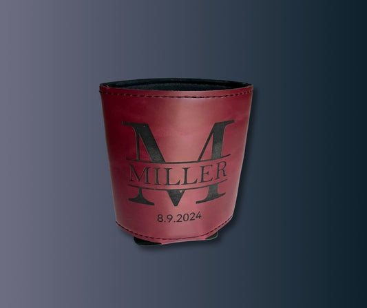 Custom maroon leatherette koozie engraved with large letter M, family name Miller, and date 8.9.2024, shown against dark background.