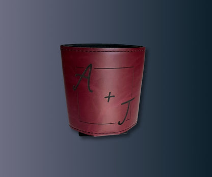 Personalized leatherette koozie in maroon with engraved initials A + J, stitched edges, displayed on dark background.