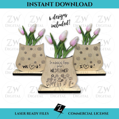 Three laser-cut layered wooden vases made from birch plywood, featuring engraved message of "In a field of roses, be a wildflower," "I love you," and "we love you" with scored floral details, displayed with pink tulips; one vase stands on a wooden base and the other hangs with twine.
