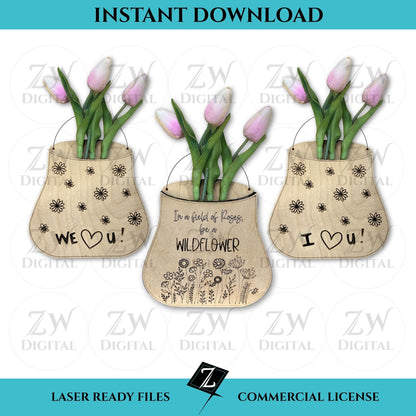Three laser-cut layered wooden vases made from birch plywood, featuring engraved message of "In a field of roses, be a wildflower," "I love you," and "we love you" with scored floral details, displayed with pink tulips; one vase stands on a wooden base and the other hangs with twine.