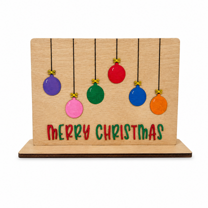 Finished wooden Christmas ornament tabletop sign featuring six colorful hanging ornaments and red and green “Merry Christmas” lettering on a display base.