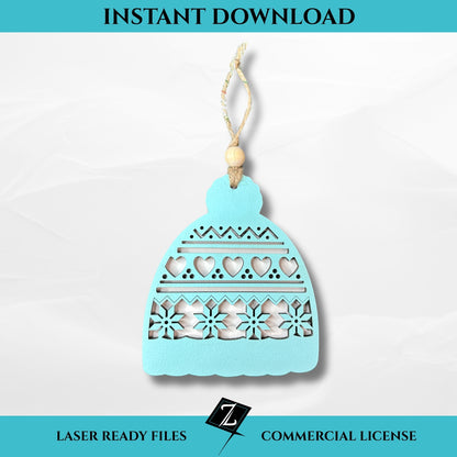 Layered laser-cut ornament shaped like a winter hat with hearts, zigzags, and snowflake cutout details, painted light blue and topped with a wooden bead and string hanger.