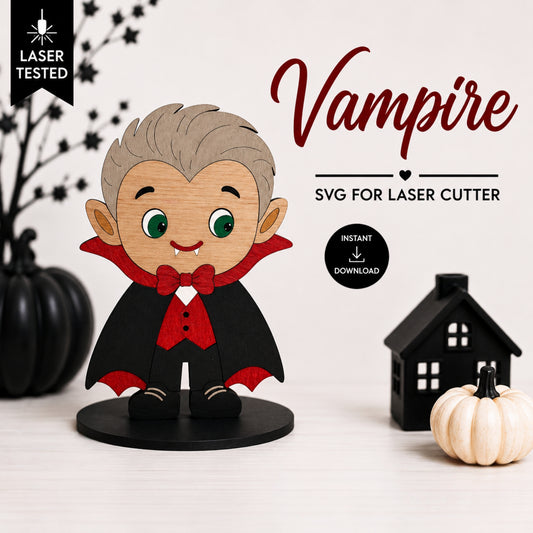 A cute chibi vampire SVG cut file design displayed on a wooden base, surrounded by Halloween props including black pumpkins, a small black house, and a white pumpkin on a white background. Text overlays read 'Vampire SVG FOR LASER CUTTER' with 'Laser Tested' and 'Instant Download' badges.