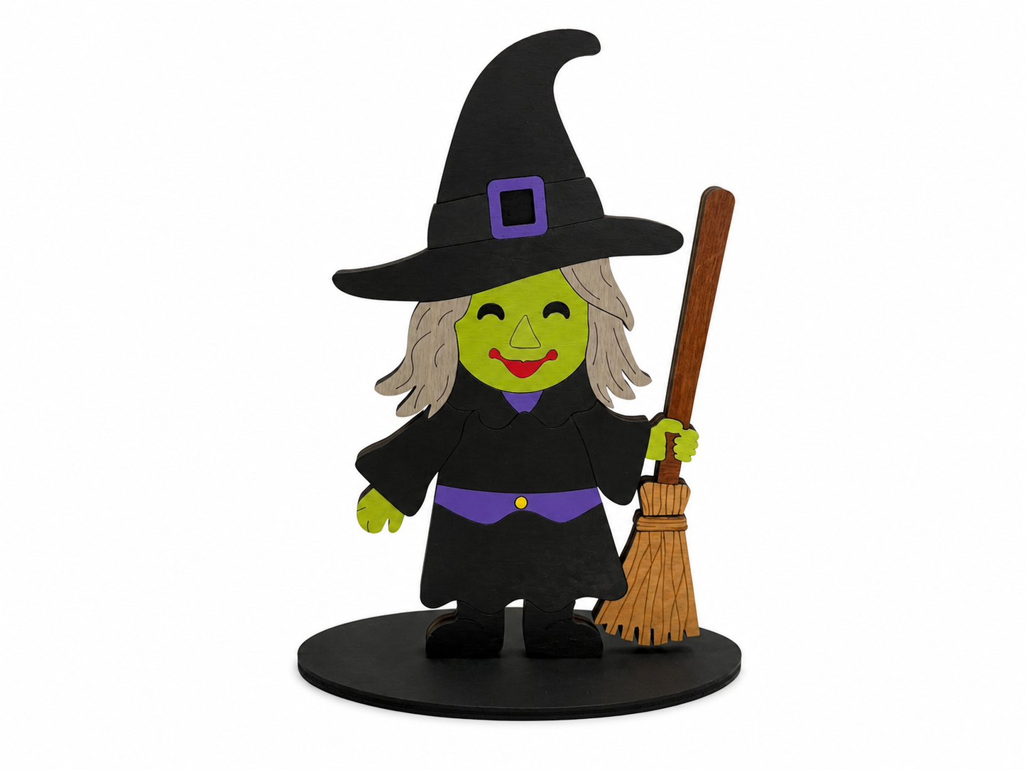 A stylized wooden cutout of a smiling witch character wearing a black hat and robe with purple accents, holding a brown broomstick on a round black base against a plain white background.