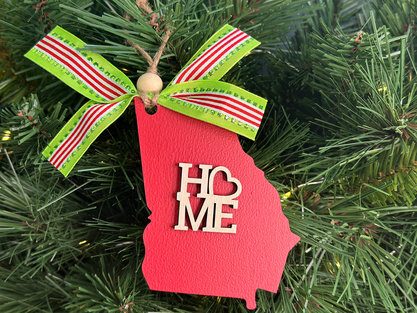 Red wooden Christmas ornament in the shape of the state of Georgia and with the word "Home" in natural wood.  Adorned with a green, red, and white ribbon and wooden bead on twine for easy hanging. 