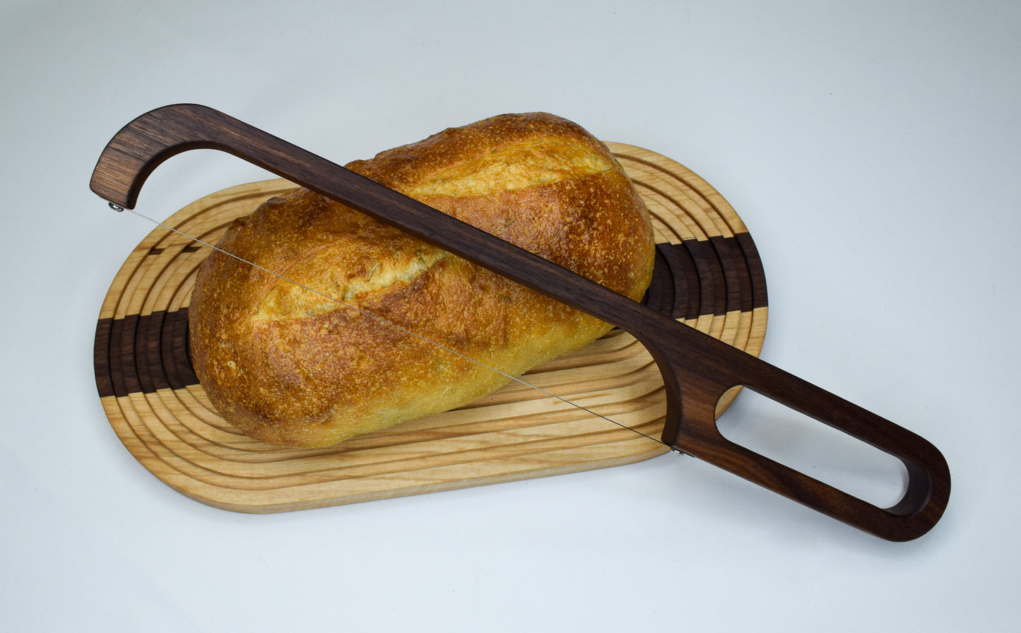 Handmade wood bread board made with maple and walnut woods. Bread board is featuring a loaf of bread and a bow knife.