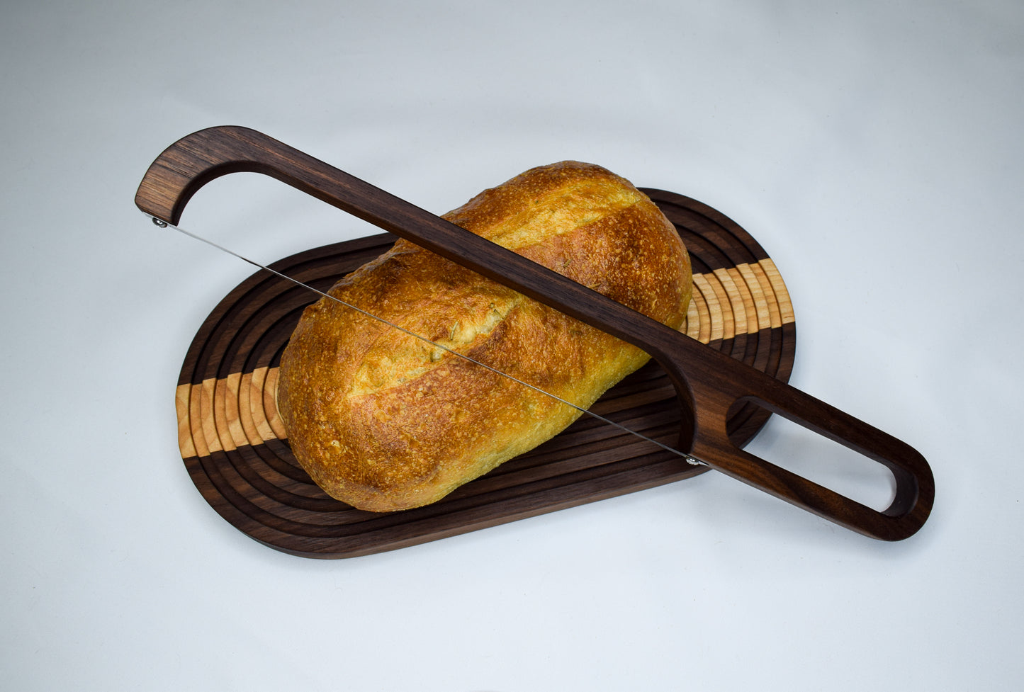 A beautifully handmade bread board featuring a loaf of break and a bread bow knife made from wood.