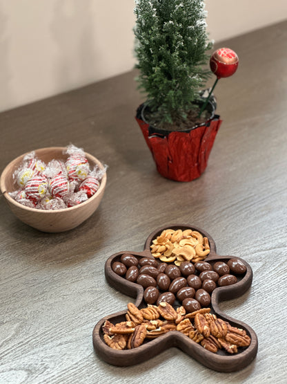 Handmade wood serving tray in the shape of a gingerbread man. On display with nuts and chocolates.