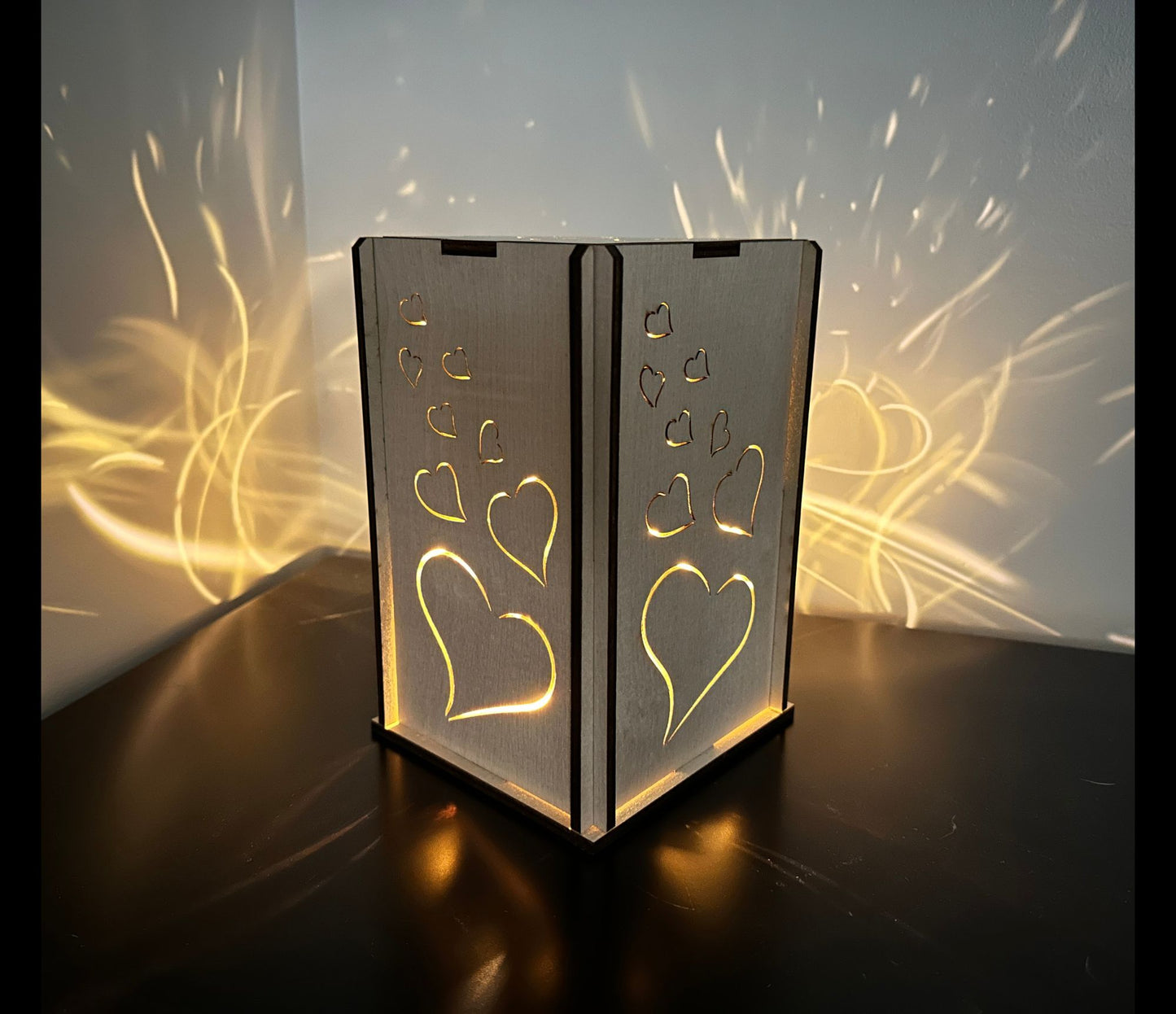 A handmade wood lantern with a heart design that cascades a whimsical light pattern on the wall.