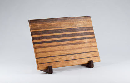 Ombre striped cutting board with alternating walnut and cherry wood. Cutting board displayed on handmade, wooden stand.