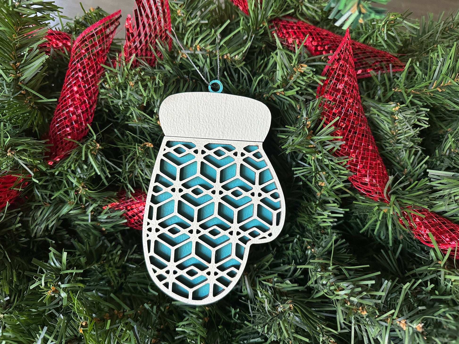 A blue, wooden, handmade Christmas ornament in the shape of a mitten.