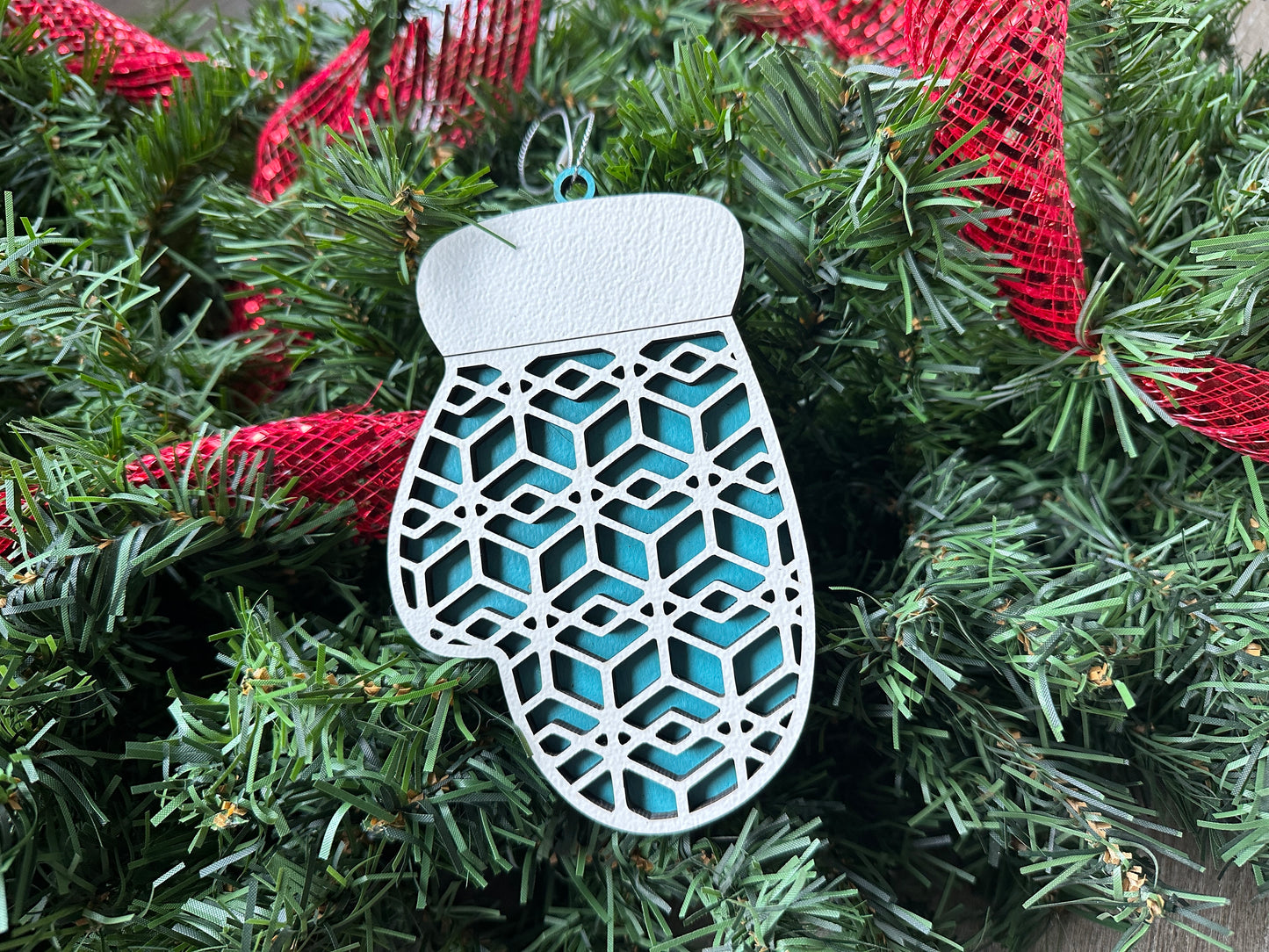 Handmade Christmas ornament in the shape of a mitten. A light blue mitten with light colored design on top.