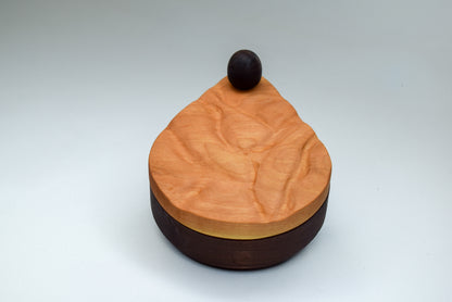 A handmade salt cellar being displayed closed. Made with cherry wood, the cellar is shaped like a teardrop.