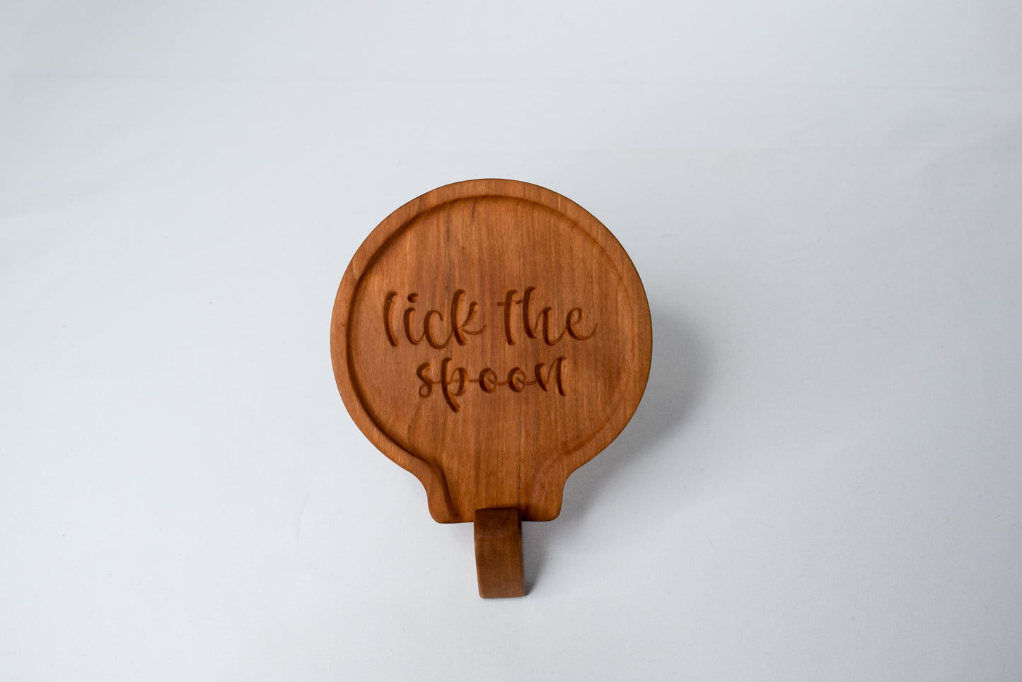 A fun gift idea for those who love to cook - a handmade wooden spoon rest with the saying "lick the spoon" and made out of cherry wood.