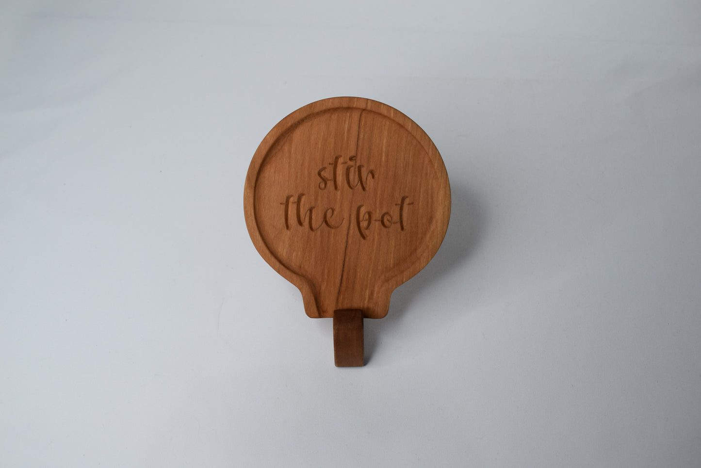 A fun gift idea for those who love to cook - a handmade wooden spoon rest with the saying "stir the pot" made out of cherry wood.