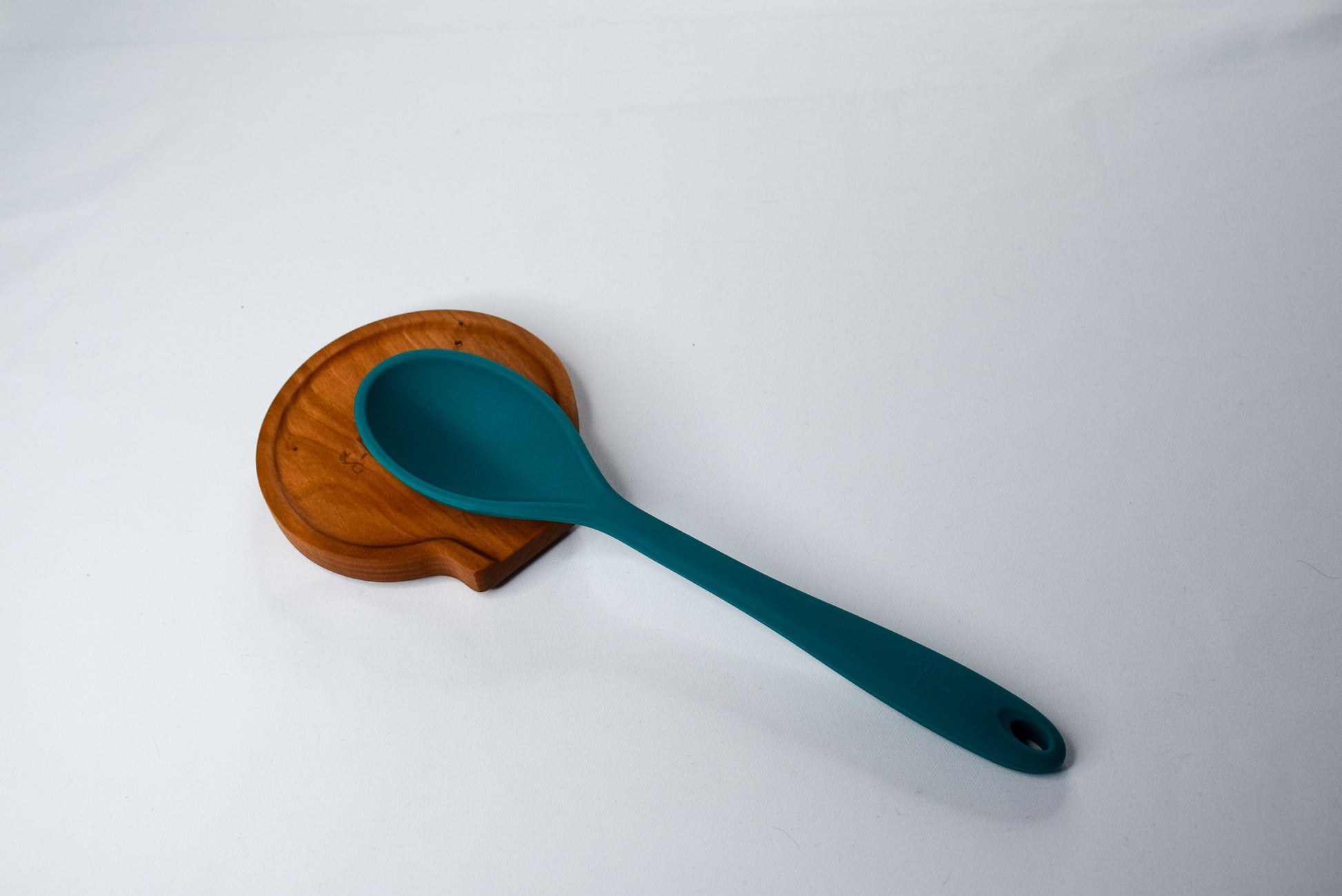 A handmade wooden spoon rest displayed with a kitchen spoon resting on it.