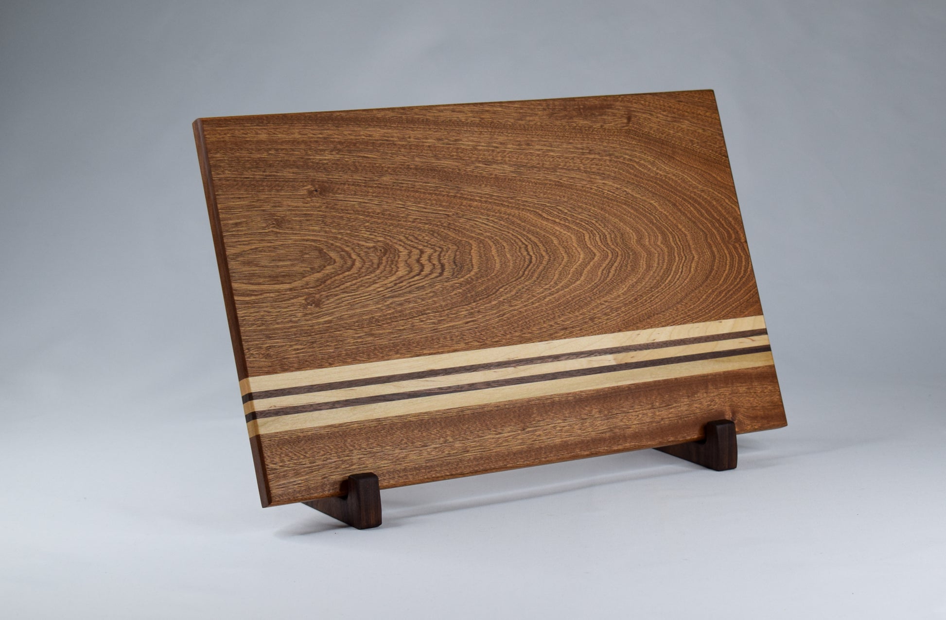 Beautiful handmade cutting board with simple alternating stripes of maple and walnut hardwoods against a sapele hardwood backdrop.