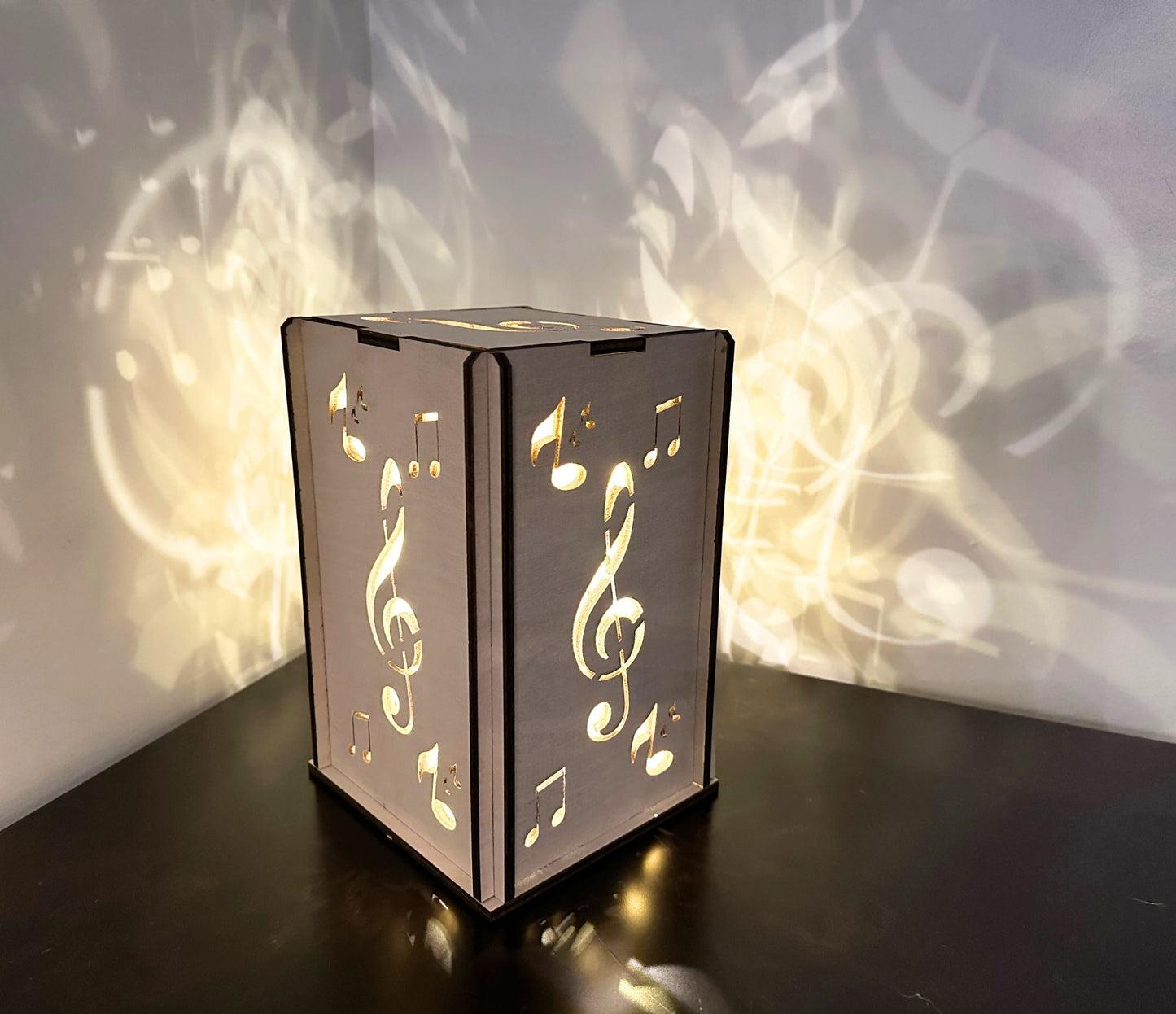 A wooden lantern handmade with music notes on it -- cascading a whimsical design on the wall when lit up.