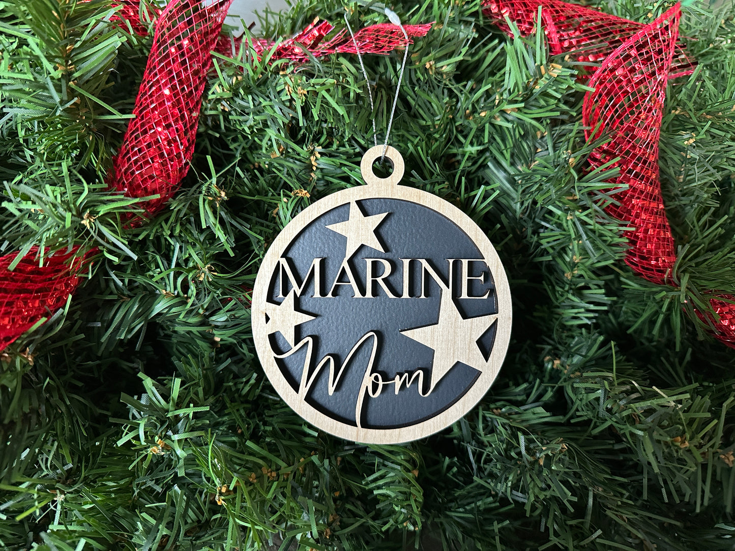 Handmade wood Christmas ornament. Black ornament with light colored birchwood words on top. Words read "Marine Mom"