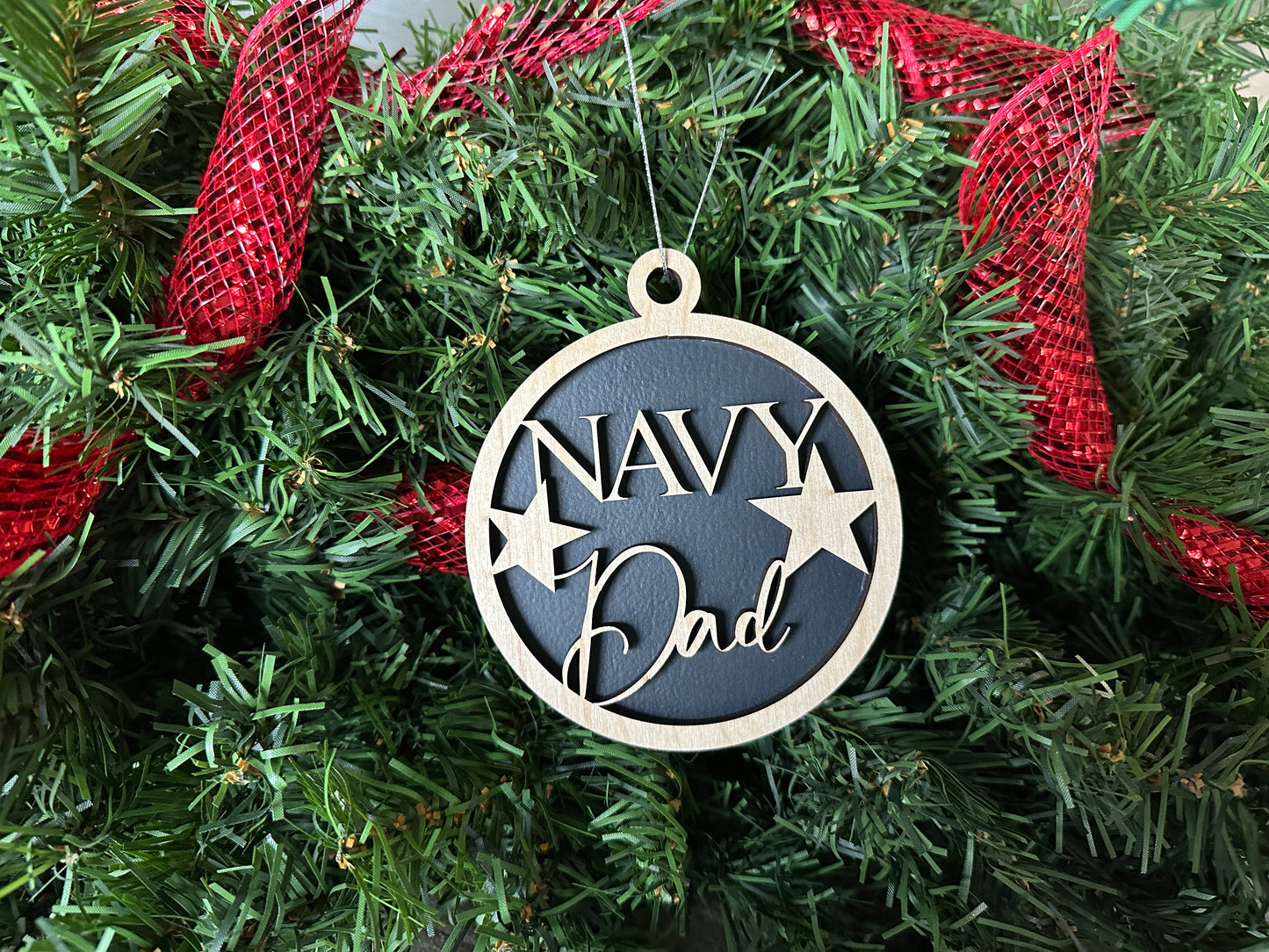 Handmade wood Christmas ornament. Black ornament with light colored birchwood words on top. Words read "Navy Dad."