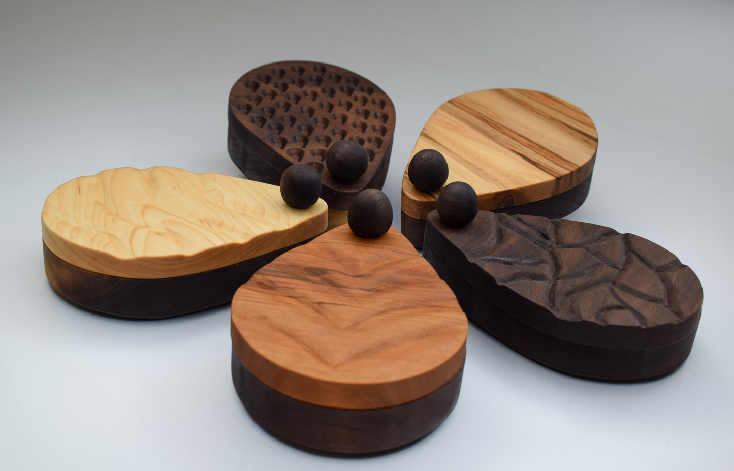 A display of 5 different salt cellars placed in a circle. Each with a different wood color and engraved design.