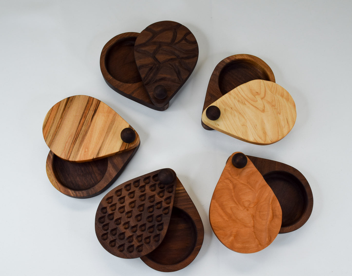 5 different handmade wooden salt cellars all displayed with their twist open tops open.